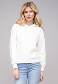 Felpa bianca con cappuccio, dal fit rilassato, maniche lunghe e orlo a costine. Abbinata a jeans azzurri per creare un contrasto. Texture liscia.
