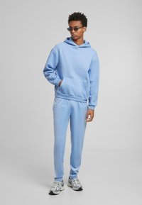 Felpa con cappuccio azzurro chiaro con tasca frontale abbinata a pantaloni jogger coordinati. Tessuto morbido, vestibilità rilassata e polsini a coste. Design sportivo.
