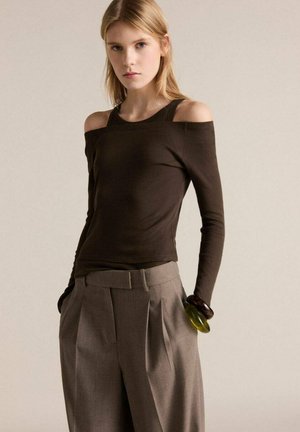 Long-sleeve, off-shoulder top in dark brown cotton fabric, paired with high-waisted, pleated gray trousers. Smooth texture and minimalist design.