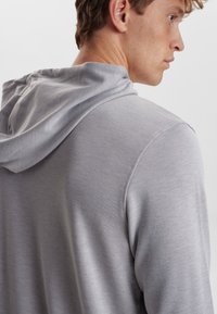 Lys grå hættetrøje med en glat tekstur, der har snore til hætten og lange ærmer. Simpelt design med minimale syninger og uden synlige mønstre.