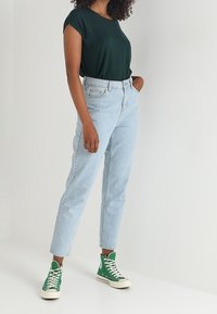 Grön kortärmad topp, ljusblå högmidjade jeans och gröna höga sneakers. Slät tyg och klassisk denimdesign med en avslappnad passform.