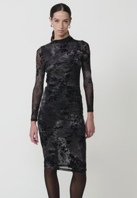 Rochie din dantelă florală neagră cu mâneci lungi, siluetă ajustată, textură transparentă și tiv la nivelul genunchilor. Prezintă un model de gradient subtil.