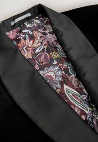 Zwarte stoffen kraag met een voering in bloemmotief in tinten bordeaux, roze en groen. Glad textuur met een satijnen afwerking.