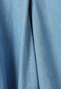 Ανοιχτό μπλε denim ύφασμα με ορατές ραφές και φυσικά πτυχώσεις που δημιουργούν απαλά σκιάσεις και υφή.