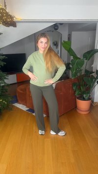 Olivgrön sweatshirt med långa ärmar, kombinerad med mörkgröna vida byxor. Vita sneakers med svarta detaljer. Inomhusmiljö med växter.