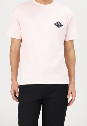 Hellrosa Baumwoll-T-Shirt mit kurzen Ärmeln, rundem Ausschnitt und einem dunkelblauen Diamant-Logo mit der Aufschrift "TOMMY JEANS" auf der Brust.