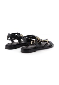 Sandali in pelle nera caratterizzati da più cinturini e dettagli in metallo con fibbie, con suola piatta e design minimalista.