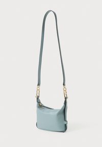 Bolsa de couro azul clara com uma textura suave, apresentando alças em corrente dourada e uma abertura com zíper para armazenamento seguro.