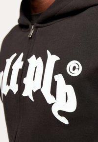 Black zip-up hoodie featuring bold white text graphic on the front, with a smooth texture and a subtle sheen.