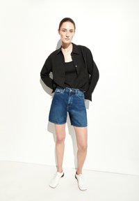 Shorts en denim bleu taille haute, associés à une chemise noire à boutons et des chaussures blanches. Le tissu est lisse avec des détails de couture visibles.