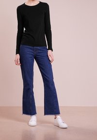 Musta pitkähihainen toppi yhdistettynä sinisiin risarusteisiin farkkuihin ja valkoisiin lenkkareihin. Yksinkertainen muotoilu, pehmeä tekstuuri ja normaali mitoitus.