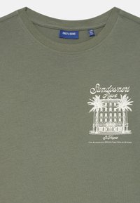 Olivegrünes Baumwoll-T-Shirt mit Rundhalsausschnitt und einem weißen Grafikdesign eines Gebäudes und Palmen, mit dem Text "Sundowners Resort".