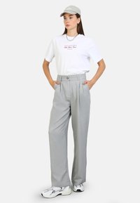 Light gray pleated trousers, white t-shirt with red text, gray cap, and white sneakers; sleek fabric with relaxed fit and side pockets.