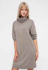 Vestido de gola alta em bege, com mangas três quartos, um corte relaxado e detalhes em ribana na bainha, feito de um tecido macio e texturizado.