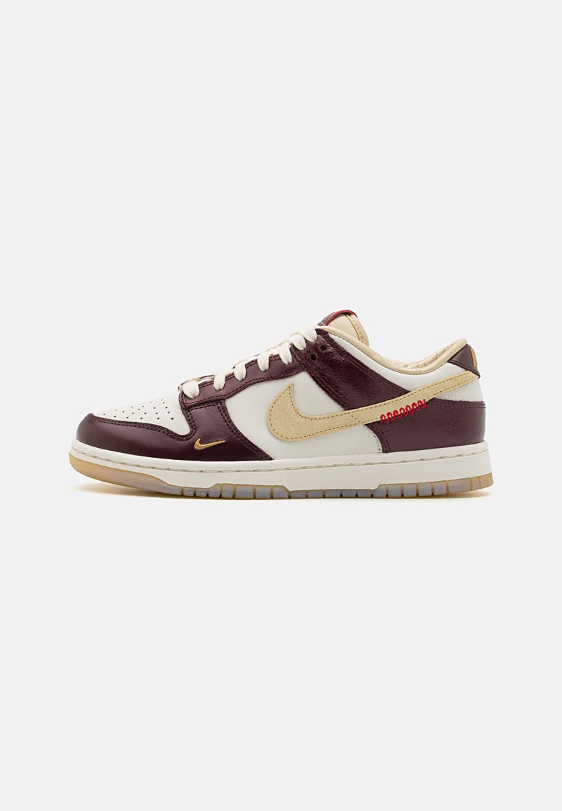 Nike Dunk Low tenisky majú burgundský a smotanový kožený zvršok, zlaté akcenty, perforovaný biely špičkový box a gumovú podrážku s trakciou.