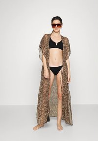 Quimono transparente com estampa de leopardo, abertura frontal, mangas curtas e fendas laterais, usado sobre um biquíni preto.