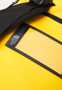 Zaino impermeabile giallo con un'esterno testurizzato, dotato di spallacci neri e un pannello rettangolare nero con un design a rete esagonale.