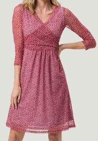 Robe imprimée avec des manches trois-quarts, décolleté en v et taille froncée. Présente un motif floral dans des teintes de rose et de rouge sur un tissu transparent.