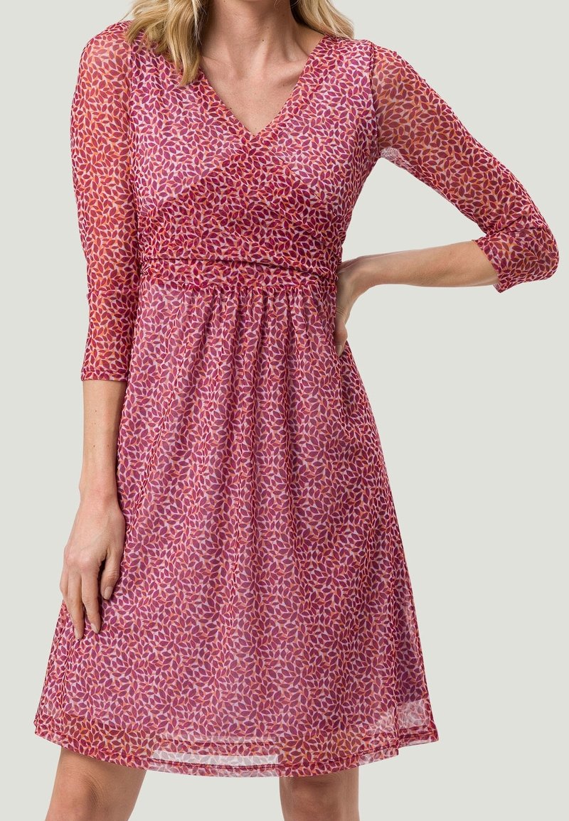 Robe imprimée avec des manches trois-quarts, décolleté en v et taille froncée. Présente un motif floral dans des teintes de rose et de rouge sur un tissu transparent.