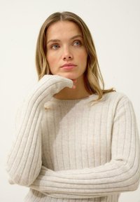 Jasnobeżowy sweter w prążki z długimi rękawami i okrągłym dekoltem, wykonany z miękkiego, teksturowanego materiału.