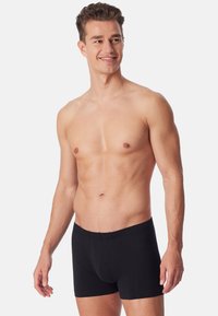 Boxer short neri realizzati in un tessuto morbido e elastico, dotati di un elastico in vita e di una vestibilità aderente, presentati su un modello maschile.