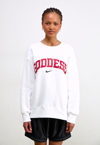 Valkoinen huppari, jossa on punaisella kirjoitettu sana "GODDESS" ja musta Nike-logo. Pehmeää materiaalia, ylihavittava malli, ribbagehuulet ja helma. Mustat shortsit.