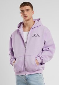 Lila zip-up dukserica s prednjim džepovima, s rebrastim manžetama i rubom. Išijani "KANI" logo na lijevoj strani prsiju. Mekana tekstura tkanine.