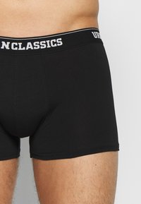 Schwarze Baumwoll-Boxershorts mit einem breiten elastischen Bund, der den Markennamen "UNCLASSICS" in weißer Schrift trägt. Eng anliegendes Design mit glatter Textur.
