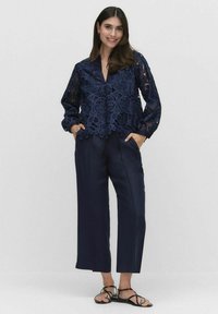 Granatowa bluzka koronkowa z długim rękawem, dekoltem w serek i kwiatowym wzorem. Połączona z granatowymi spodniami o szerokiej nogawce i czarnymi płaskimi sandałami.