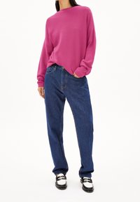 Pull en maille fuchsia à coupe décontractée, associé à un jean bleu ample. La tenue est complétée par des mocassins noirs avec des accents blancs.