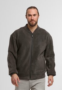 Giacca in pile grigio scuro con colletto rialzato, chiusura frontale con zip a tutta lunghezza e tasche laterali. La superficie liscia e la vestibilità comoda conferiscono un aspetto informale.