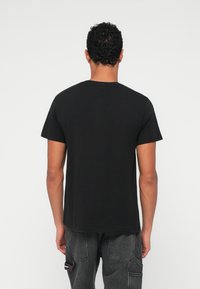 Μαύρο βαμβακερό T-shirt με κοντά μανίκια, λαιμόκοψη και λεία υφή. Χωρίς ορατά γραφικά ή σχέδια. Πίσω όψη σε απλό φόντο.