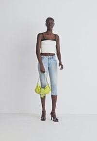 Haut court blanc avec des bretelles noires, jeans courts bleu clair, et un petit sac à main jaune avec un détail de boucle. Sandales à talons noires avec des clous.