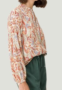 Blusa de manga larga en tejido ligero con un patrón de paisley multicolor, cuello redondo y mangas fruncidas, combinada con pantalones verdes.
