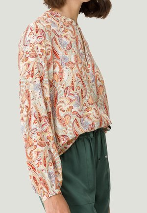 Blouse à manches longues en tissu léger avec un motif paisley multicolore, un col rond et des manches gathers, associée à un pantalon vert.