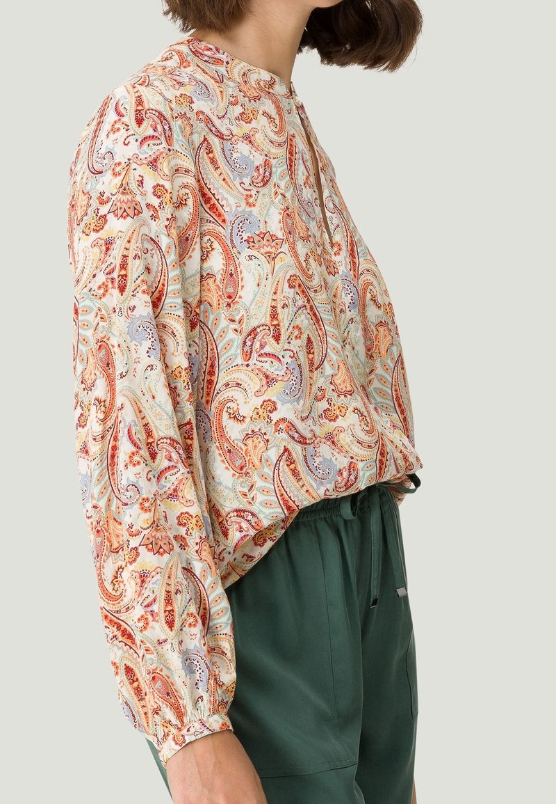 Blusa de manga larga en tejido ligero con un patrón de paisley multicolor, cuello redondo y mangas fruncidas, combinada con pantalones verdes.