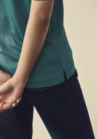 T-shirt en coton teal avec une coupe décontractée, fentes latérales à l'ourlet. Associé à un pantalon bleu marine, présentant des détails de couture subtils.