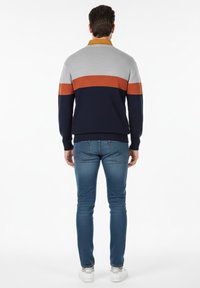 Suéter de hombre en gris, naranja y marino con textura acanalada. Presenta un cuello y un diseño a bloques de color. Combinado con jeans azules.