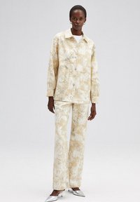 Crème en beige gestreepte jas met bijpassende broek, gemaakt van textuurstof. Beschikt over grote zakken en een kraaghalslijn. Zilveren schoenen.