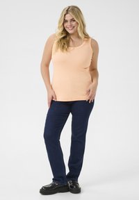 Light peach ribbed tank top paired with dark blue straight-leg jeans and black platform shoes, set against a neutral background.