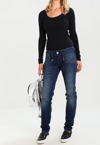 Jeans in denim skinny-fit di lavaggio blu scuro. Abbinati a un top nero slim a maniche lunghe e semplici scarpe slip-on nere e bianche. Borsa argentata.
