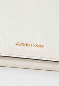 Valge tekstuuriga nahast rahakott, millel on kuldne "MICHAEL KORS" logo, omades peent disaini ja õmmeldud servi. Minimalistlik ja funktsionaalne.