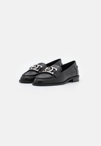 Des mocassins en cuir noir arborent un bout arrondi, une boucle décorative en argent, des coutures raffinées et un petit talon bloc pour plus de stabilité.