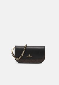 Pochette Michael Kors noire et marron avec une bandoulière chaîne dorée et un logo sur le devant, sur un fond gris clair uni.