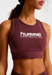 Vinröd atletisk crop top av mjukt, texturerat tyg med rund halsringning och vit "hummel PERFORMANCE"-logotyp tryckt i mitten.