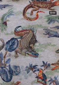 Tejido gris con ilustraciones coloridas de reptiles y plantas tropicales. Los detalles notables incluyen un cocodrilo y un tucán entre el follaje.