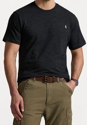 Mann trägt ein eng anliegendes schwarzes T-Shirt mit kurzen Ärmeln, kleinem weißem Logo, Khaki-Cargohosen, braunem Gürtel und Uhr.