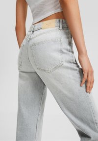 Pantalones de mezclilla de un gris claro y de cintura alta, con bolsillos traseros y una etiqueta de cuero. La tela tiene un aspecto ligeramente desgastado y texturizado.