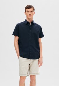 Kortärmad marinblå skjorta med en knapp-down krage, tillverkad av vävt tyg. Matchad med ljusbeige, uppvikta shorts. Enkel, strukturerad design.