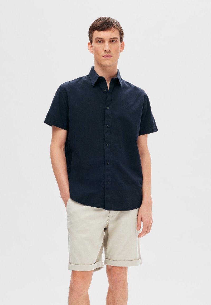 Kortärmad marinblå skjorta med en knapp-down krage, tillverkad av vävt tyg. Matchad med ljusbeige, uppvikta shorts. Enkel, strukturerad design.